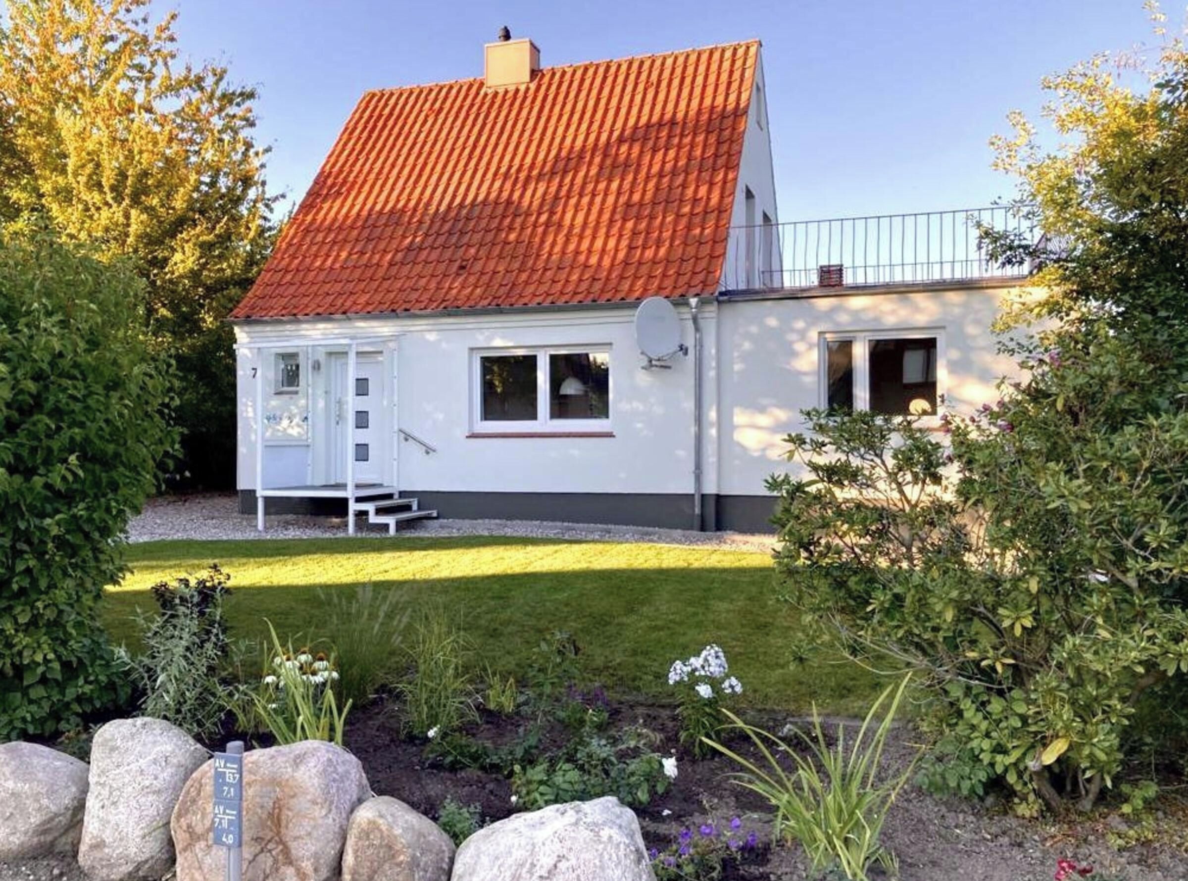 A white house with a red roof, a satellite dish, and a small porch.