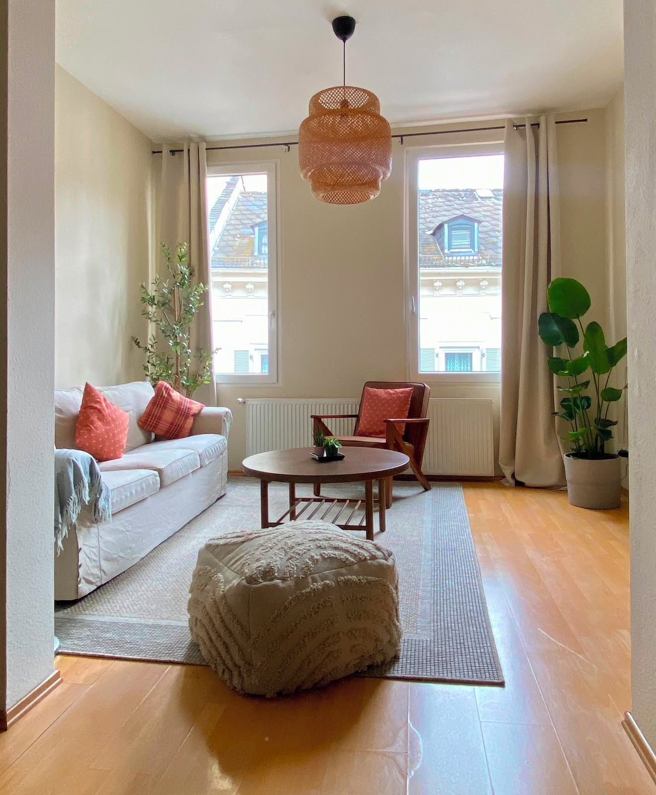 Una sala de estar con un sofá, una mesa redonda de centro, una silla, una lámpara colgante y una planta en maceta.