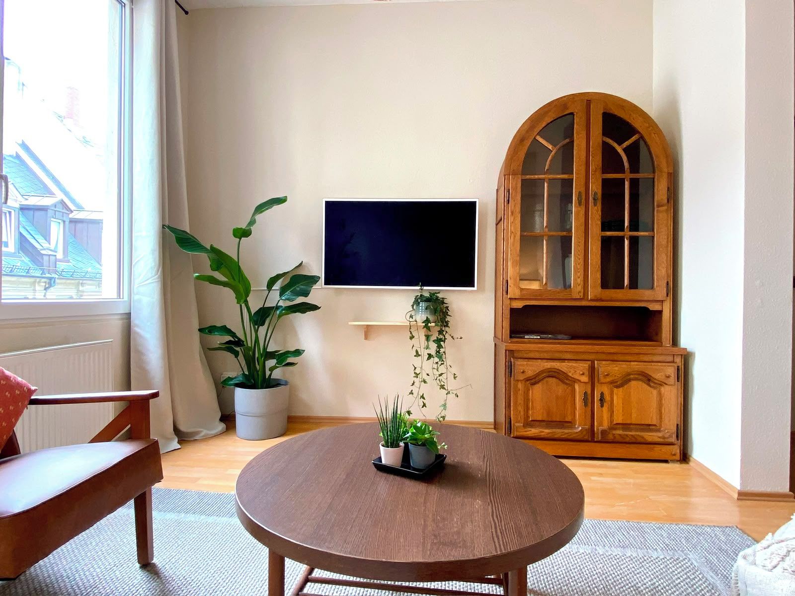 A living room with a round wooden table, a potted plant, a flat-screen TV, and a wooden cabinet.