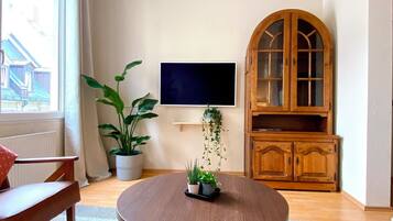 A living room with a round wooden table, a potted plant, a flat-screen TV, and a wooden cabinet.