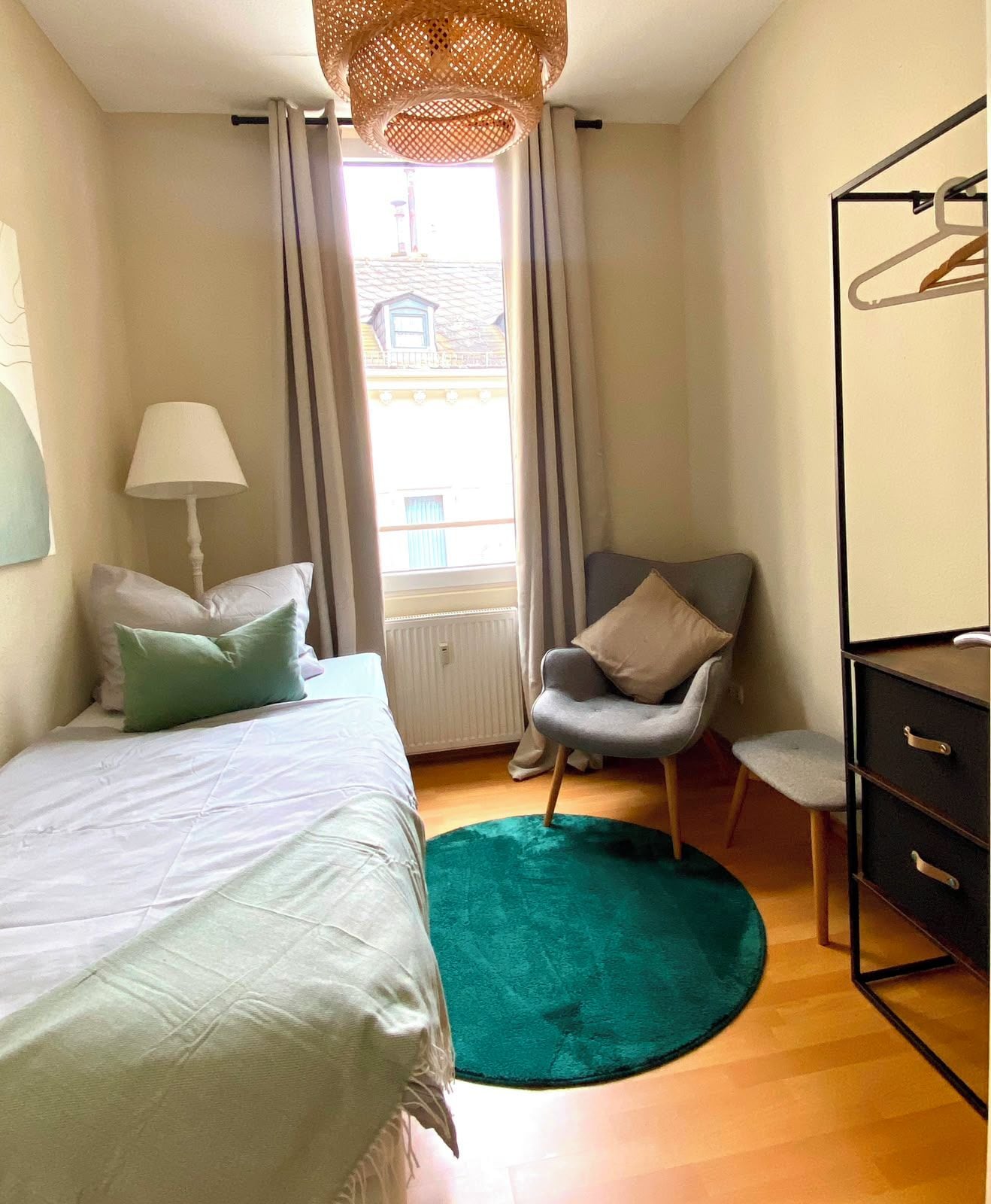 Ein Schlafzimmer mit einem Bett, einem Sessel, einer Kommode und einem Fenster mit Vorhängen.