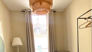 A bedroom with a bed, a chair, a dresser, and a window with curtains. - Charming Old Town Apartment in Wiesbaden, 2 Bedrooms, Parking Garage 150 m Away (Wiesbaden)