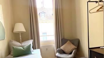 Ein Schlafzimmer mit einem Bett, einem Sessel, einer Kommode und einem Fenster mit Vorhängen.