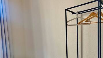 A room with a blue armchair, a small stool, a dark dresser with drawers, and a hanging clothes rack.