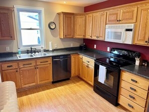 A kitchen with wooden cabinets, a stainless steel dishwasher, a black stove, and a microwave. - Agate Bay Getaway - Short Walk to Lake Superior & Downtown (Two Harbors)