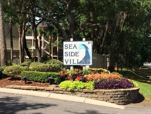 A sign for Sea Side Villas with a view of a landscaped area and a building in the background. - Direct Oceanfront: Million Dollar Sunrise Views & Steps to Coligny (Hilton Head Island)