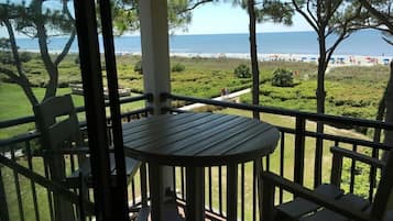 A balcony with a table and chairs, overlooking a beach with people and umbrellas.