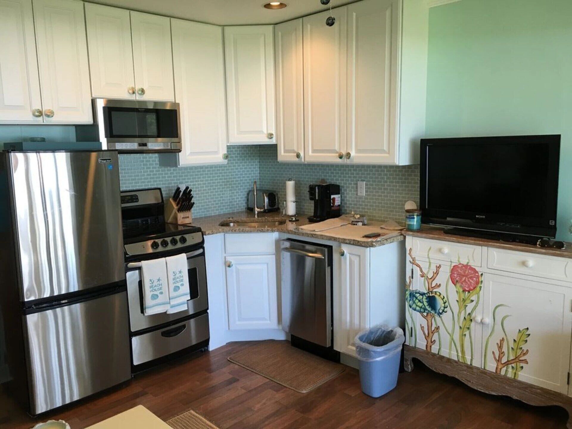 A compact kitchen with stainless steel appliances, white cabinets, a microwave, a toaster, and a television.