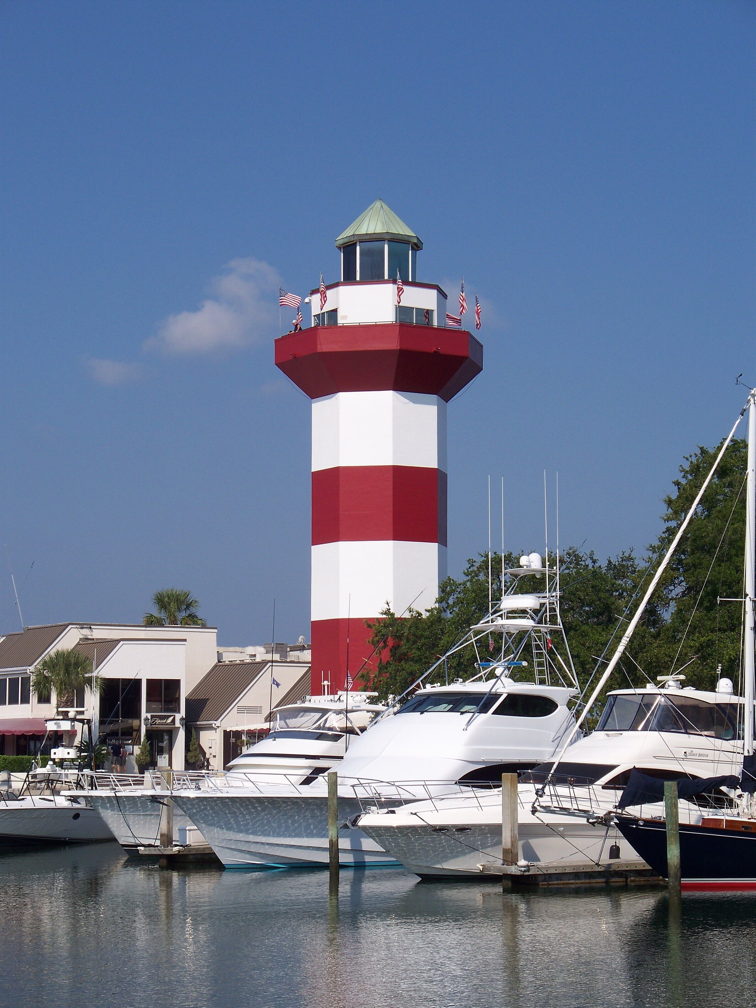 A lighthouse with a red and white striped tower, surrounded by boats docked at a marina.
