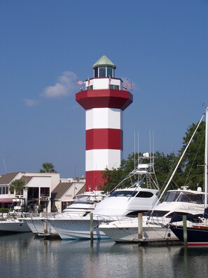 Un far amb una torre de franges vermelles i blanques, envoltat de vaixells amarrats a una marina.