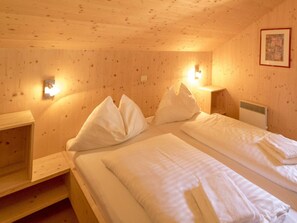 Ein Zimmer aus Holz mit zwei Betten, Kissen, einem Nachttisch und Wandleuchten.