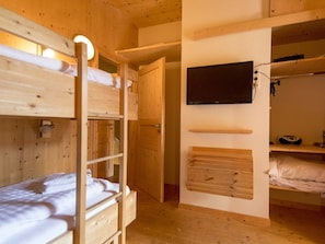 Habitación con literas de madera y un televisor fijado a la pared.