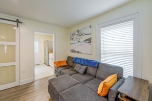 A living room with a grey sofa, orange cushions, a blue throw, and a painting of a beach scene.