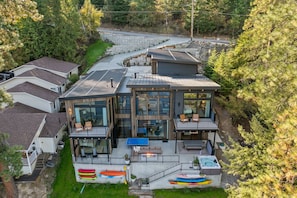 Ein modernes, zweistöckiges Haus mit einer großen Terrasse, Sitzmöbeln im Freien und Kajaks.