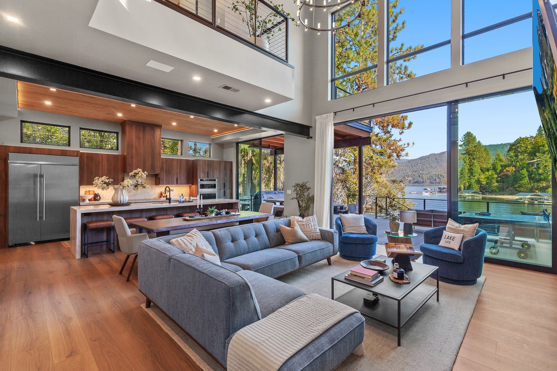 A modern interior with a kitchen, dining area, and seating by a large window overlooking a lake.
