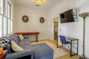 Ein Wohnzimmer mit einem Ecksofa, einem an der Wand montierten Flachbildfernseher, einem Esstisch mit Stühlen und einer dekorativen Lampe.