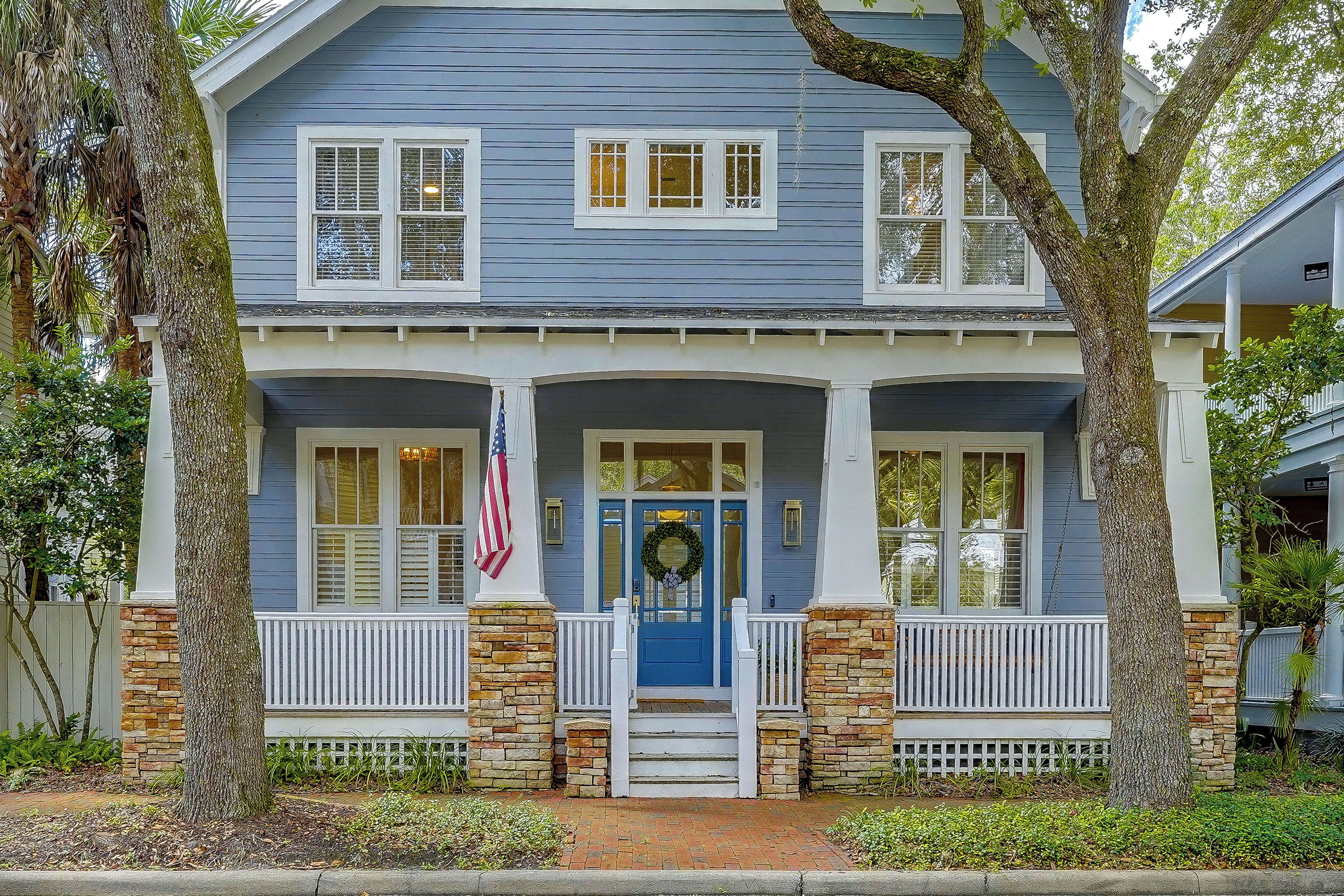 A two-story house with a blue exterior, white shutters, and a front porch with a brick column.