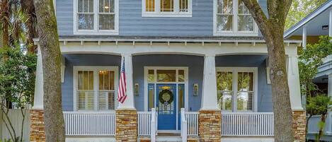 A two-story house with a blue exterior, white shutters, and a front porch with a brick column.