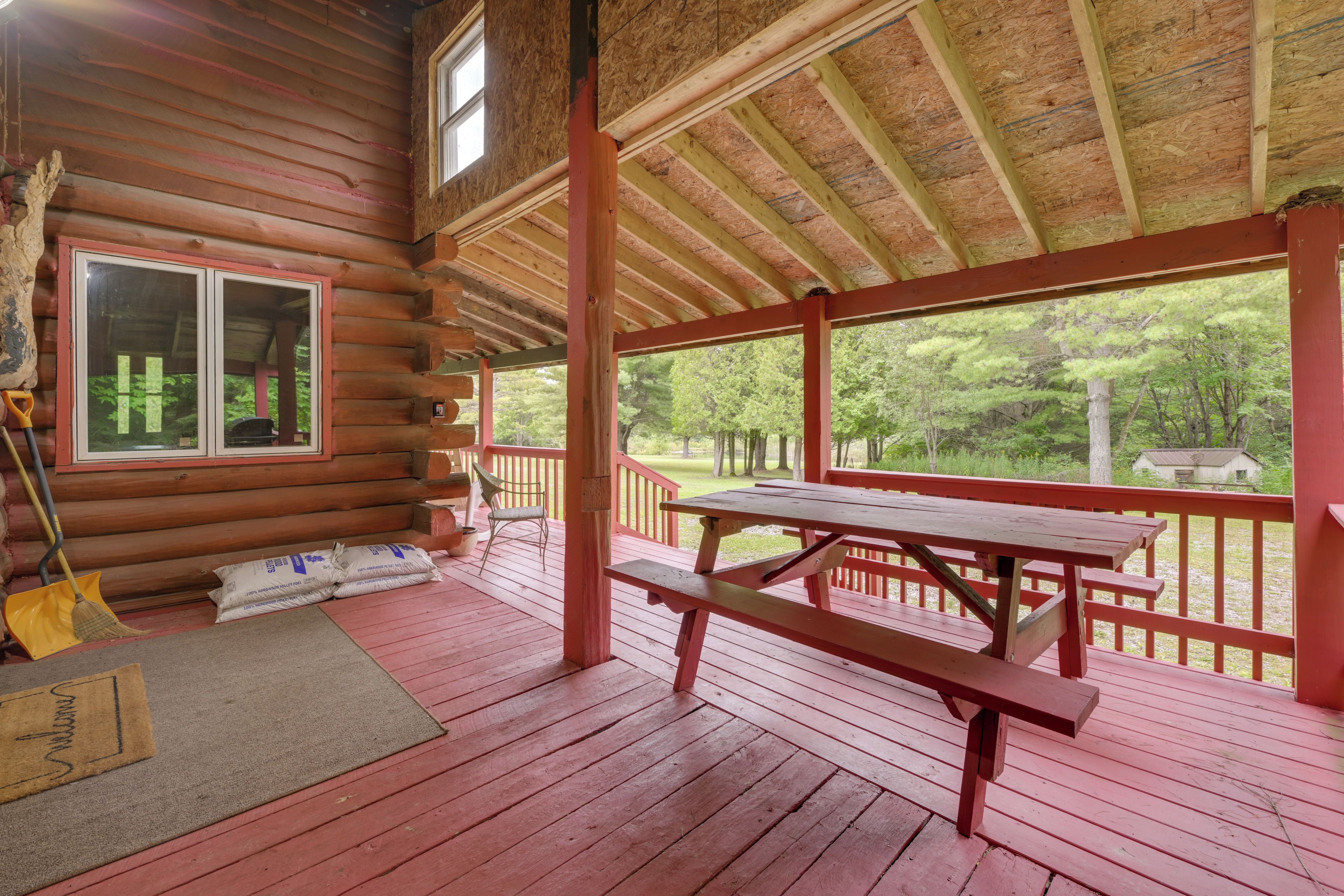 A wooden cabin with a covered porch, a picnic table, and a view of the surrounding forest.