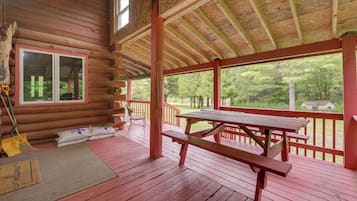 A wooden cabin with a covered porch, a picnic table, and a view of the surrounding forest.