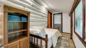 A bedroom with a wooden wardrobe, a bed with white bedding, and a window with blinds.