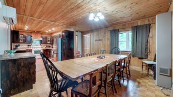 A spacious kitchen with wooden cabinets, a large dining table, and a window with curtains.