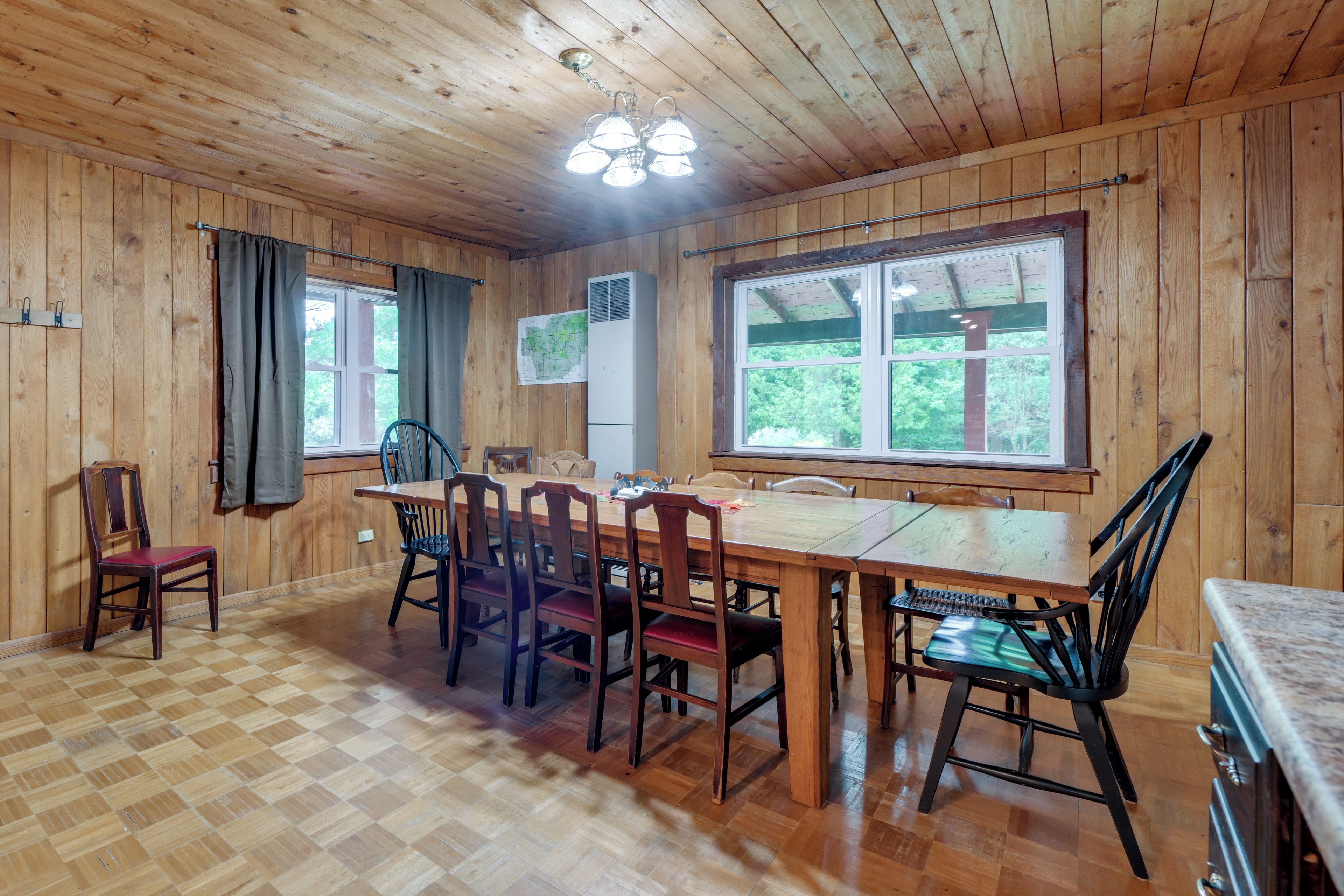 A wooden interior with a dining table, chairs, a ceiling fan, and large windows.