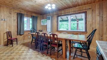 A wooden interior with a dining table, chairs, a ceiling fan, and large windows.