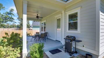 A covered patio with a ceiling fan, a barbecue grill, and a dining table with chairs.