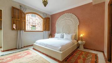 Een slaapkamer met een groot bed, een decoratief hoofdeinde, een nachtkastje met een lamp en een raam met gordijnen.