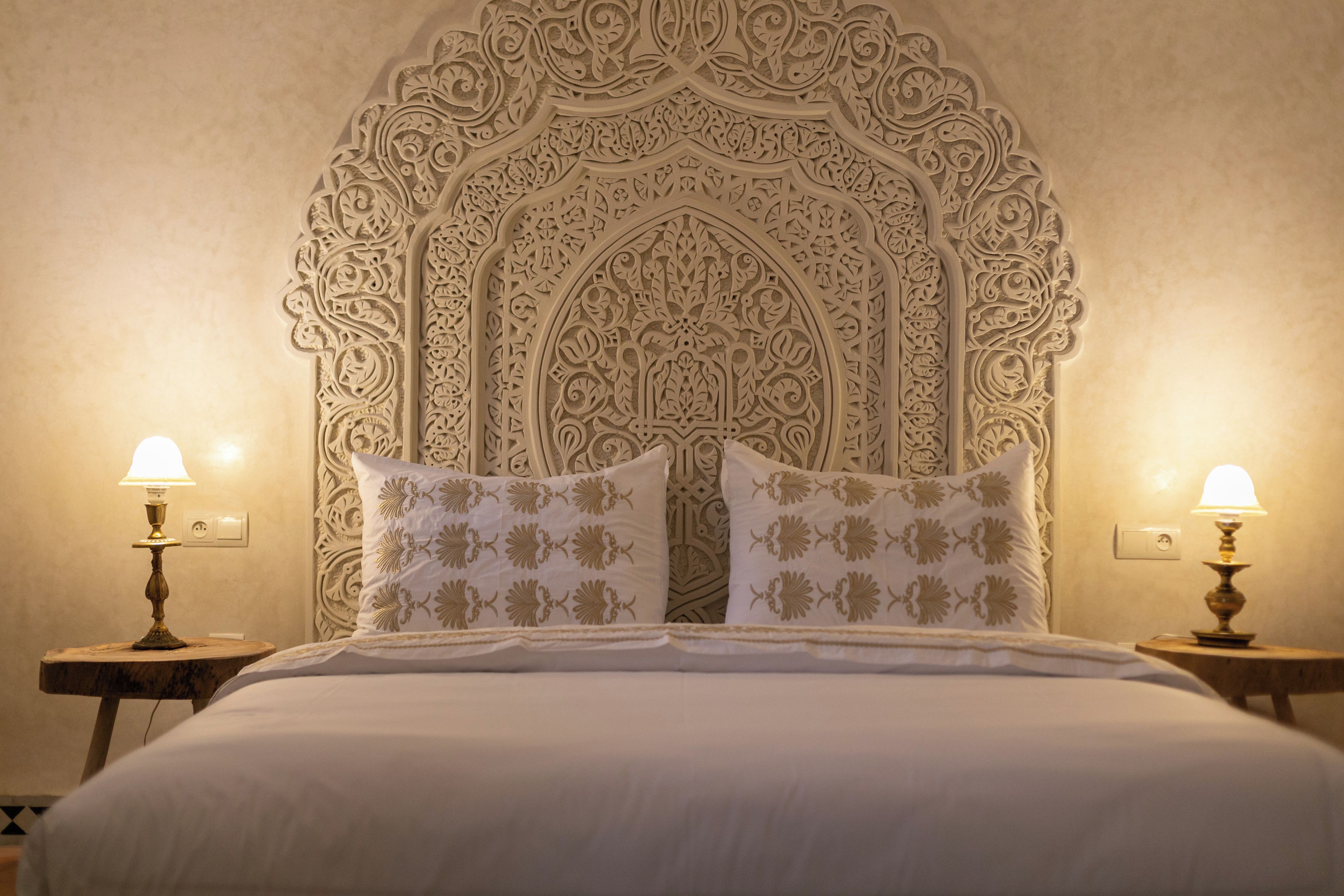 A bed with a decorative headboard, two bedside lamps, and matching pillows.