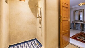 Ein Badezimmer mit Dusche, einer Fußmatte mit Schachmuster und einer Holztür zu einem weiteren Raum.