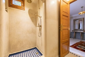 A bathroom with a shower, a checkered floor mat, and a wooden door leading to another room. - Riad Dar Razallah  (Marrakech)