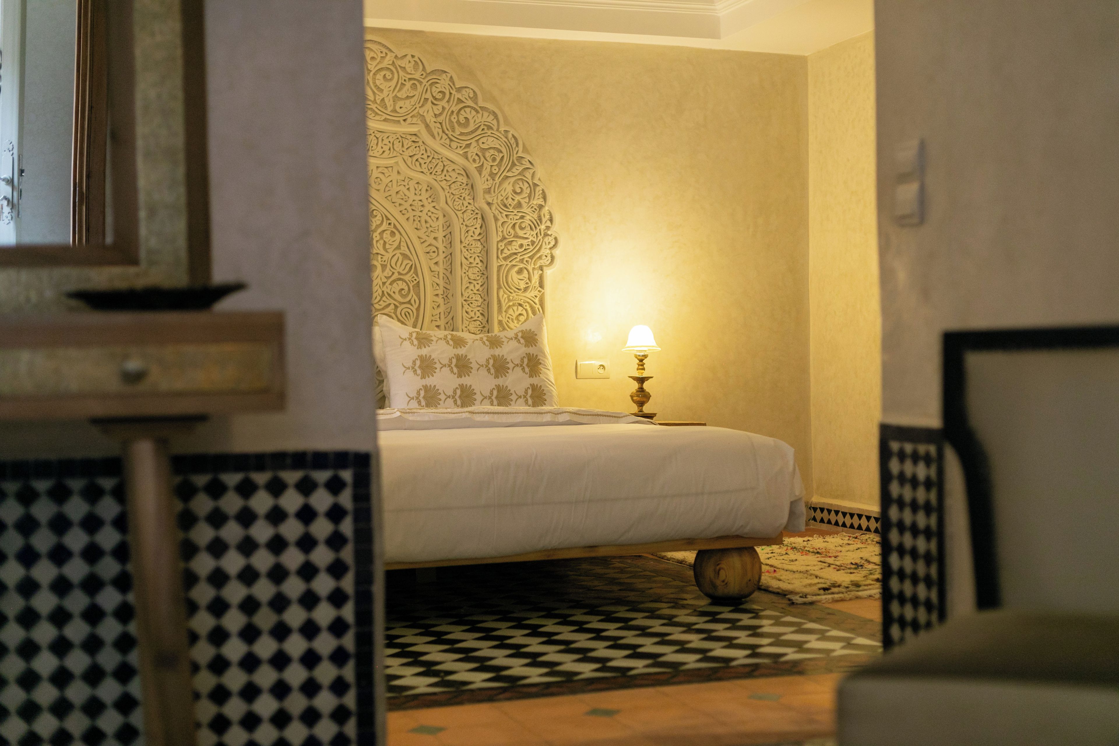 Una camera d'albergo con un letto, un comodino con una lampada e un pavimento decorato.