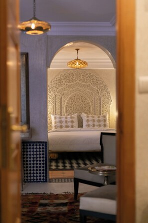 A bedroom with a bed, pillows, a nightstand, a chair, a patterned rug, and a decorative ceiling light. - Riad Dar Razallah  (Marrakech)