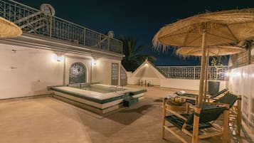 Un área de piscina en la azotea con un jacuzzi, sillones de descanso y sombrillas.