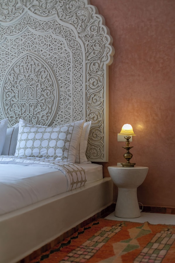 A bed with a white headboard and patterned pillows, a bedside lamp, and a patterned rug.