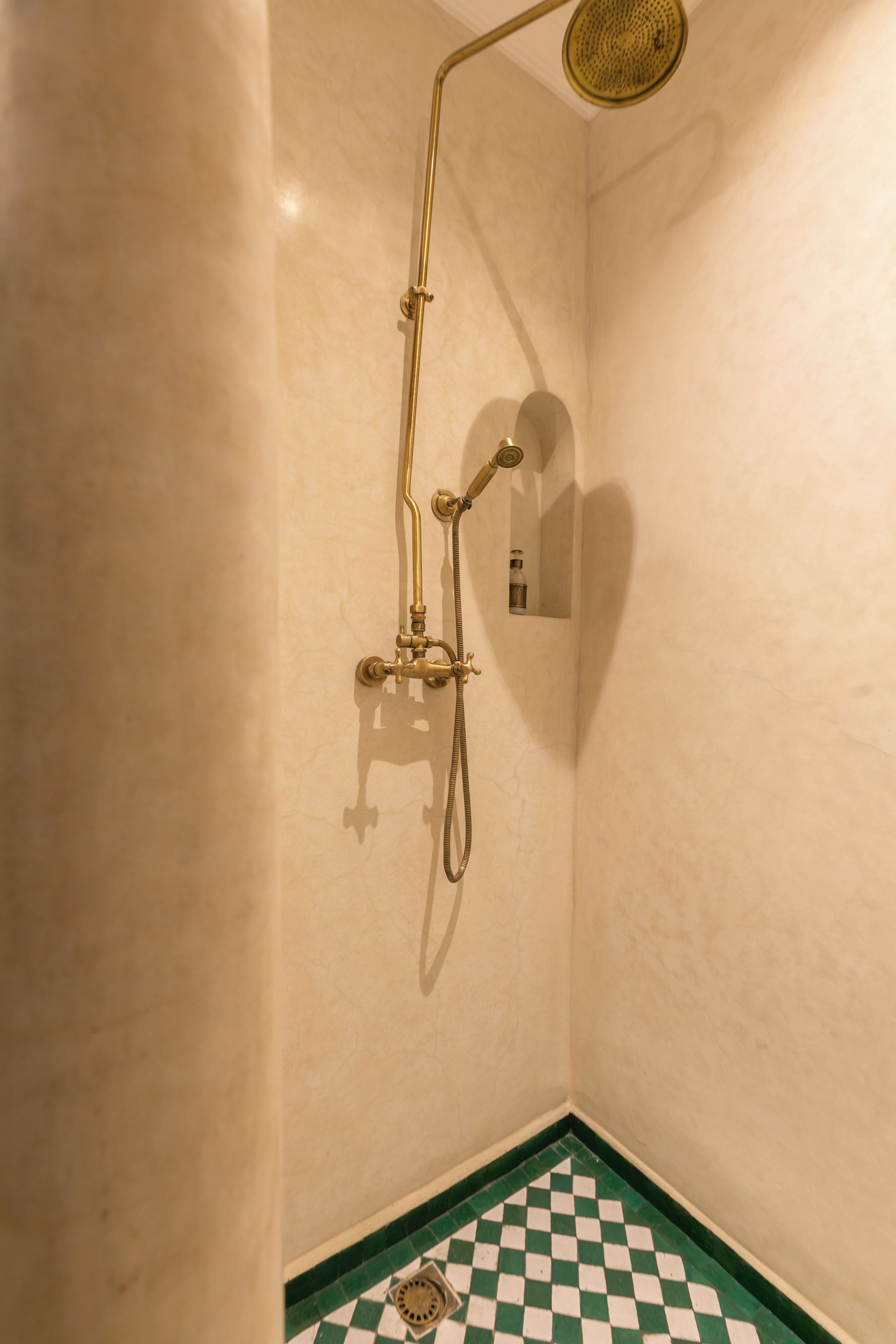 A bathroom with a checkered floor, a shower with a golden showerhead, and a wall-mounted towel rack.