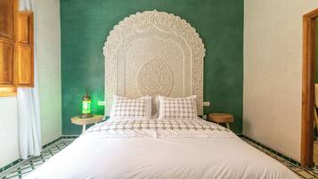 Ein Bett mit weißer Bettdecke und Kissen, eine grüne Wand und ein dekorativer Kopfteil.