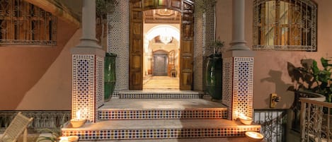A traditional Moroccan interior with a tiled entrance, a chandelier, and a staircase leading to a door.