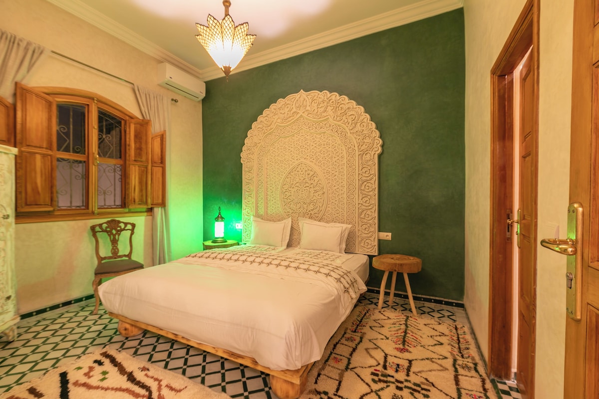 Un dormitorio con una cama grande, un cabecero decorativo, un armario de madera, una ventana con cortinas y una pared verde.