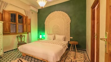 Un dormitorio con una cama grande, un cabecero decorativo, un armario de madera, una ventana con cortinas y una pared verde.
