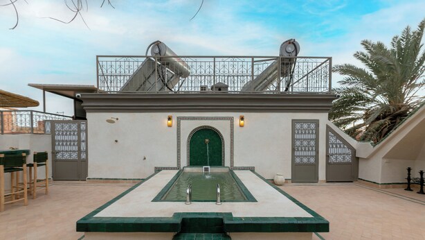 Ein Poolbereich mit einer grün gefliesten Liegefläche, einem Wasserspiel und einer überdachten Sitzgelegenheit.