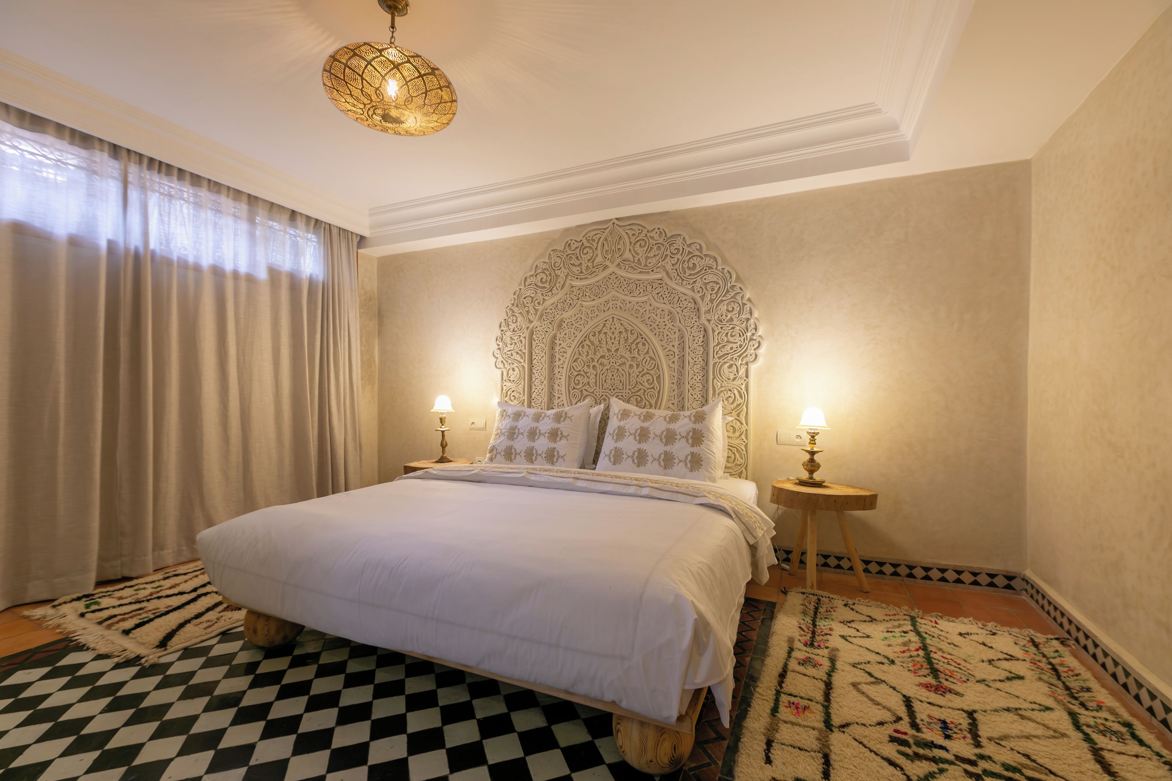 A hotel room with a large bed, two bedside lamps, a patterned rug, and a decorative headboard.