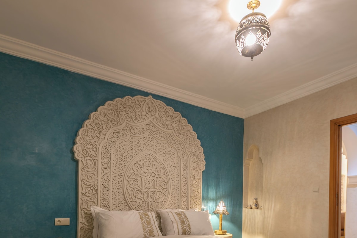 A bedroom with a large bed, a nightstand, a wall-mounted lamp, and a decorative ceiling light.