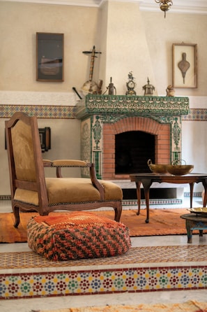 Habitación tradicional con chimenea, una silla de madera, un tapete estampado y una mesa con un cuenco de latón.