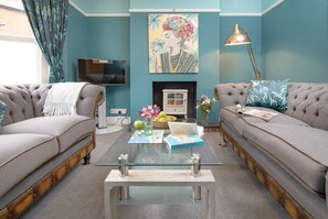 A living room with two sofas, a glass coffee table, a fireplace, a television, and a painting on the wall. - Sea Folly Luxury Townhouse, Central, Parking, Seafront 400m (Sidmouth)