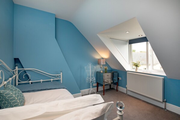 A bedroom with a sloped ceiling, a bed with white bedding, a dresser, a radiator, and a window with a view. - Sea Folly Luxury Townhouse, Central, Parking, Seafront 400m (Sidmouth)