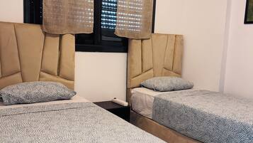 A hotel room with two beds, a nightstand, a window with blinds, and a ceiling light fixture.