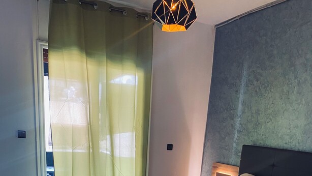 Ett modernt sovrum med en stor säng, ett sängbord, en liten rund pall och en mönstrad matta.